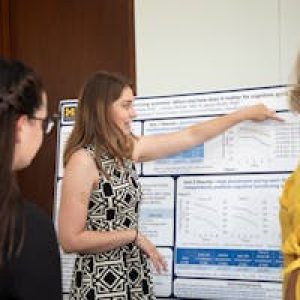 Researcher explaining cognitive science poster to peers, emphasizing scientific collaboration.