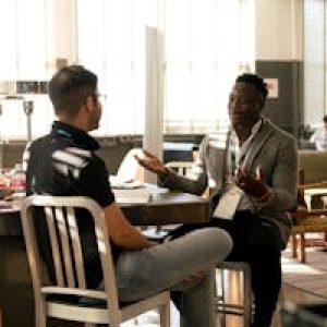 Two men having a casual discussion in a bright indoor setting, highlighting mentorship.